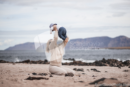 Image of Mother enjoying winter vacations holding, playing and lifting his infant baby boy son high in the air on sandy beach on Lanzarote island, Spain. Family travel and vacations concept