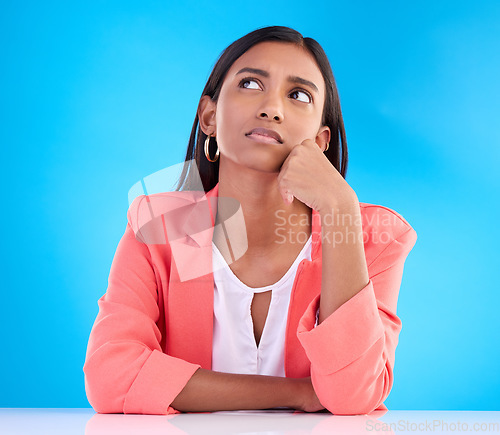 Image of Thinking, confused and a business woman on a blue background in studio for problem solving at her desk. Idea, doubt and decision with a young female employee contemplating a thought, choice or option