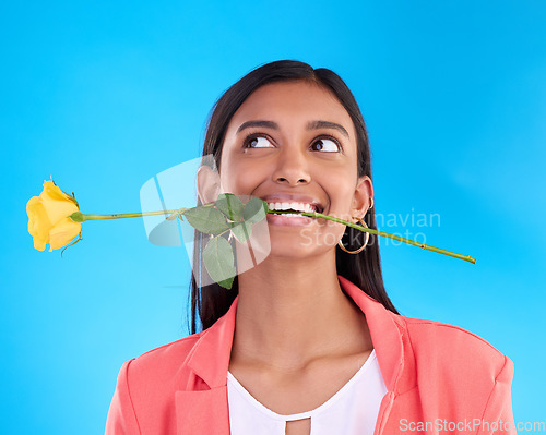 Image of Thinking, rose and valentines day with a woman on a blue background in studio for love or romance. Idea, yellow flower and romantic with an attractive young female carrying a plant in her mouth