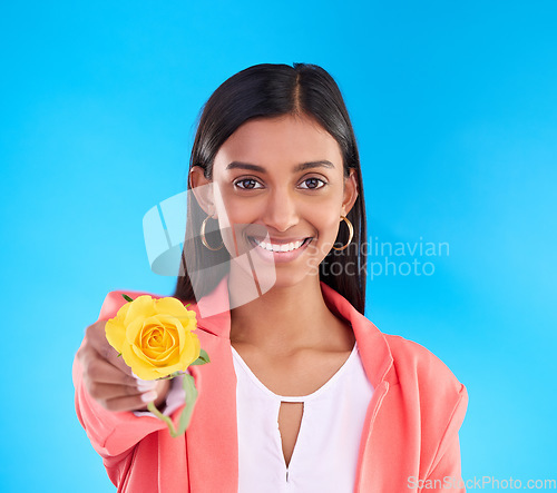 Image of Portrait, rose and valentines day with a woman on a blue background in studio for love or romance. Face, happy and smile with an attractive young female holding a yellow flower as a romantic gift