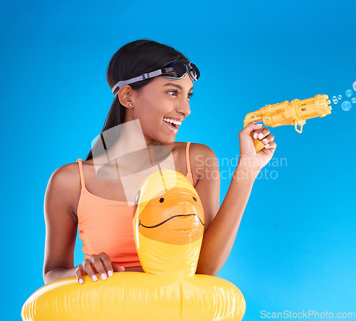 Image of Bubbles, summer swimsuit and woman with bubble gun in a studio with fun and happiness. Isolated, blue background and happy female model with playful smile and swimming outfit for pool entertainment