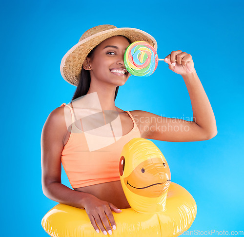 Image of Pool float, happy woman and portrait in a studio with lollipop sweet and swimsuit with a smile. Isolated, blue background and holiday outfit of a young female with happiness and candy feeling fun