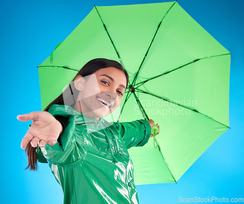 Image of Portrait, smile and woman with umbrella, excited and expression against blue studio background. Face, female and person with cover from rain, happiness and excitement with joy, adventure or insurance