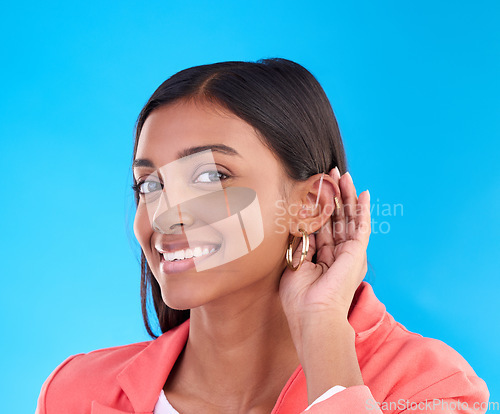 Image of Portrait, secret and gossip with a woman on a blue background in studio cupping her ear for hearing. Privacy, whisper and hand gesture with an attractive young female trying to hear news or a rumor