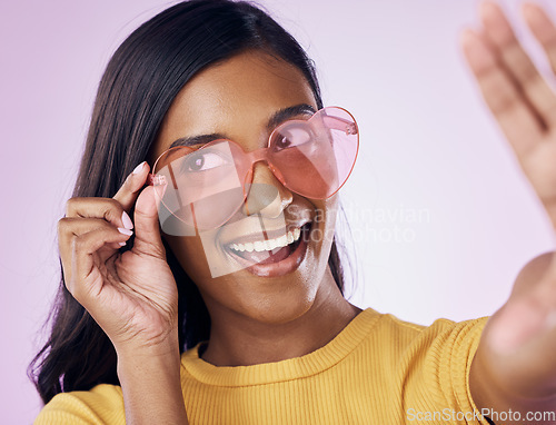 Image of Heart, glasses and selfie by indian woman in studio happy, cheerful and fun on purple background. Sunglasses, pose and female gen z fashion influencer smile for profile picture, photo or blog post