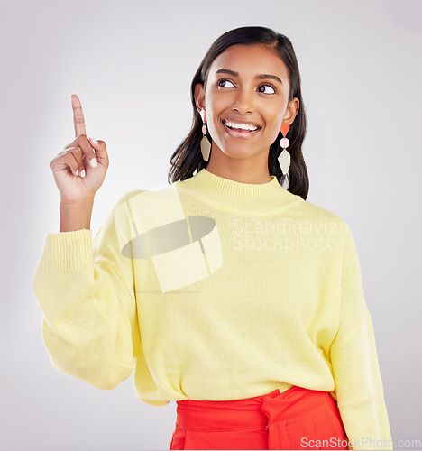 Image of Woman is pointing up, smile and marketing with announcement and product placement on studio background. Advertising, logo promo and branding with happy Indian female, show with direction and choice