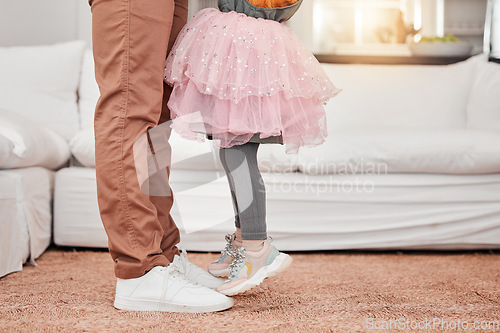 Image of Feet of father and child dancing in the living room of their modern family home to music or radio. Dance, energy and closeup of man bonding, having fun and standing with his daughter in their house.