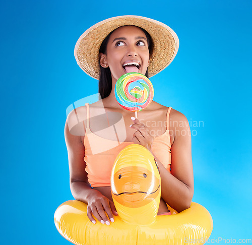 Image of Pool float, happy woman and lollipop lick in a studio with sweet, swimsuit and sweets. Isolated, blue background and holiday of a young female with happiness, licking candy and feeling funny or silly