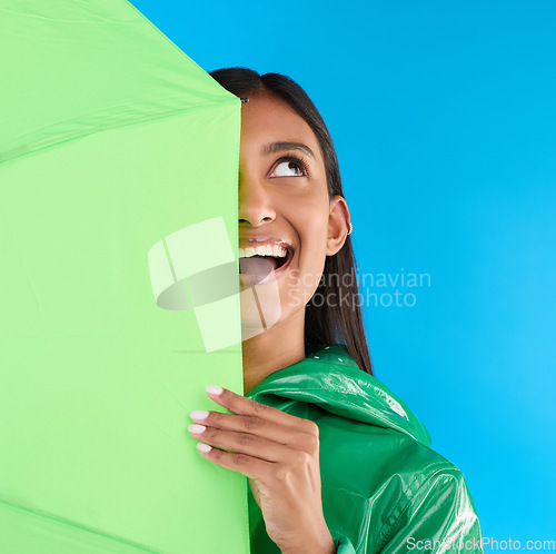 Image of Umbrella, fun or happy woman in playful studio with raincoat, silly or happiness mockup. Goofy, face or excited female on isolated blue background or looking with smile, curious or thinking expresion