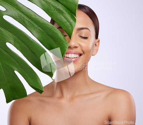 Image of Smile, leaf and woman in studio for skincare, dermatology and cosmetic on purple background. Beauty, face and girl model relax, calm and happy with glowing skin, cosmetology or monstera treatment