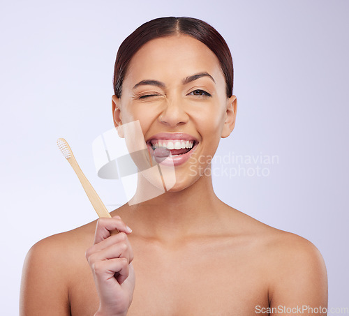 Image of Portrait, wink or happy girl brushing teeth with smile for healthy oral or dental hygiene in studio. Face, beauty or Brazilian woman model cleaning mouth with a natural bamboo wooden toothbrush