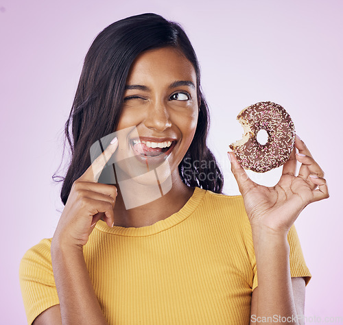 Image of Donut, dessert and wink with woman in studio for diet, snack and happiness. Sugar, food and smile with female eating chocolate treat isolated on pink background for nutrition, playful and craving