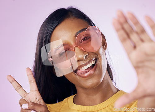 Image of Selfie, peace and indian woman in studio with heart sunglasses, cheerful or fun on purple background. Portrait, v sign and girl gen z style fashion influencer smile for profile picture or blog post