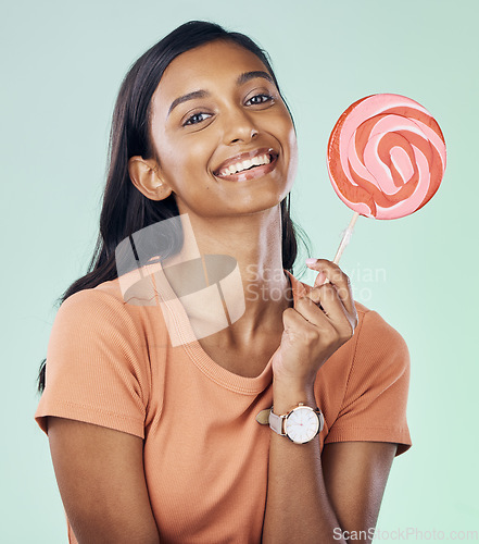 Image of Happy, lollipop portrait and studio woman with candy, junk food or dessert product for delicious snack. Happiness, smile or Indian gen z person with sweets, sucker or sugar treats on green background