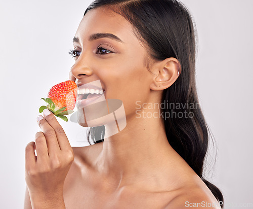 Image of Happy, healthy and a woman eating a strawberry for nutrition isolated on a white background in a studio. Smile, thinking and an Indian girl with a fruit for a diet, breakfast or vitamins from food