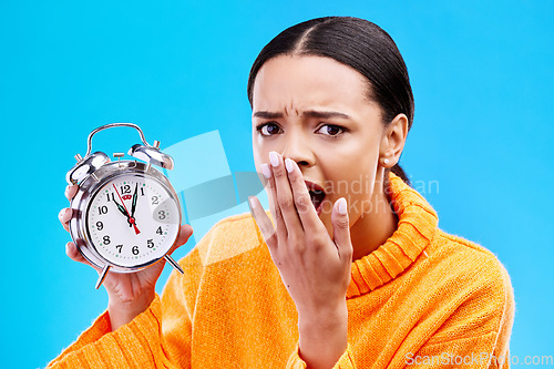 Image of Portrait, surprise and woman with an alarm clock, late and deadline with girl against a blue studio background. Face, female model and person with time, shocked and stress with schedule and wow