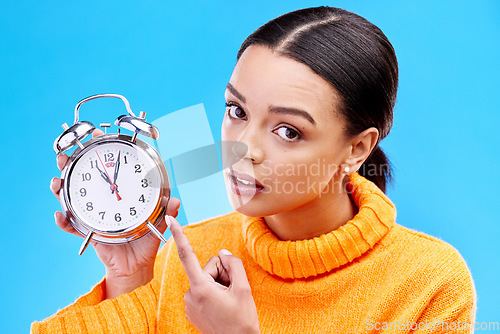 Image of Woman, annoyed and point at alarm clock in portrait for warning by blue background in studio. Gen z girl, student and model with watch, time management and schedule with angry face to start morning