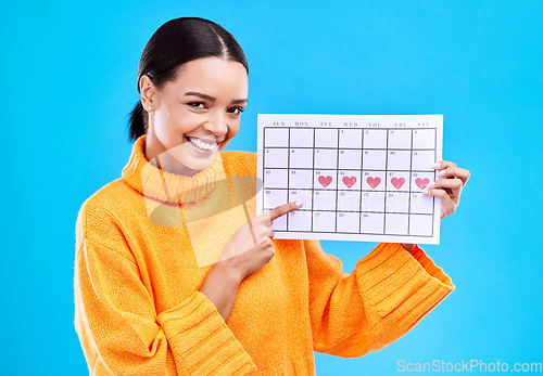 Image of Health, portrait and female with a calendar in a studio to track her menstrual or ovulation cycle. Happy, smile and face of a woman model pointing to a paper period chart isolated by blue background.