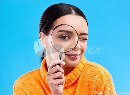 Image of Search, portrait and female with a magnifying glass in a studio for an investigation or detective cosplay. Happy, smile and headshot of a woman model with a zoom magnifier isolated by blue background