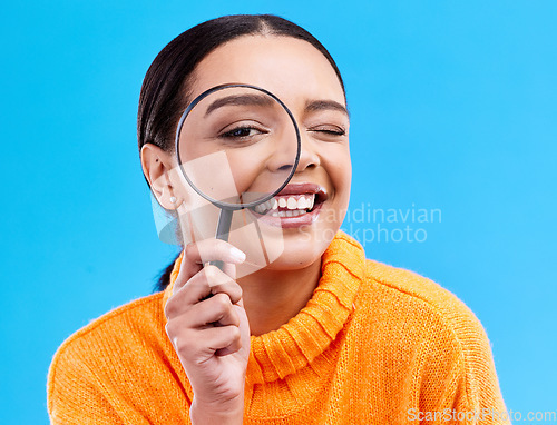 Image of Happy, portrait and female with a magnifying glass in a studio for an investigation or detective cosplay. Happiness, smile and headshot of a female model with a magnifier isolated by blue background.