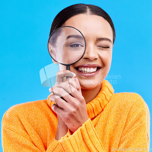 Image of Smile, portrait and woman with a magnifier in a studio for an investigation or detective cosplay. Happiness, excited and headshot of a female model with a magnifying glass isolated by blue background