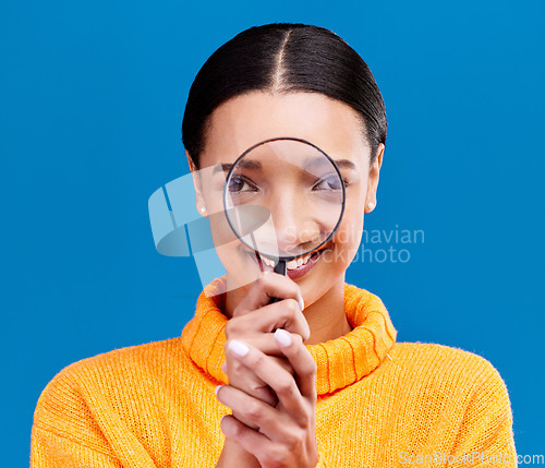 Image of Woman, magnifying glass and smile in studio portrait with funny face, search and zoom by blue background. Gen z girl, investigation and research with lens for study, inspection and check by backdrop