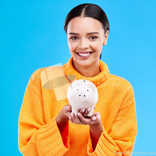 Image of Happy woman, money and piggy bank for investment, budget or finance against a blue studio background. Portrait of female smile holding savings, cash or coin for profit, investing or financial freedom