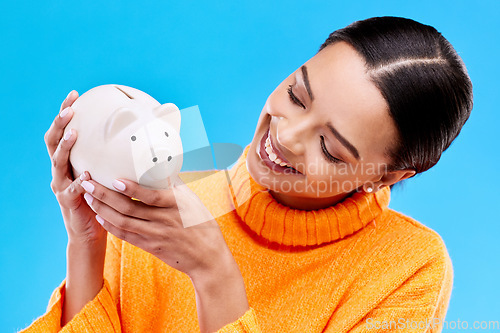 Image of Happy woman, money and piggy bank for investment, budget or finance against a blue studio background. Female smile holding savings of cash or coin for change, profit or investing in financial freedom