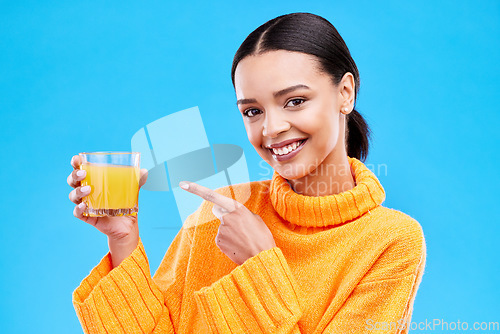 Image of Happy woman, portrait and pointing to orange juice in studio, blue background and backdrop. Female model, drinking glass and fruit cocktail beverage for nutrition, diet and detox health of vitamin c