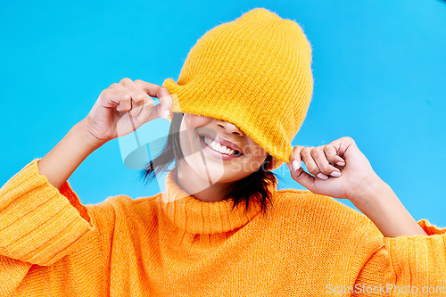 Image of Fashion, happy and hide with woman and beanie in studio for cover, winter and goofy. Playful, happiness and smile with female and knitted hat isolated on blue background for funny, silly and cool