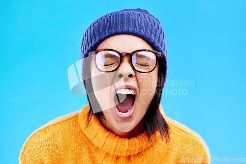 Image of Portrait of woman in winter fashion, screaming with beanie and glasses isolated on blue background. Anger, frustration and face of frustrated gen z girl in studio with warm clothes for cold weather.