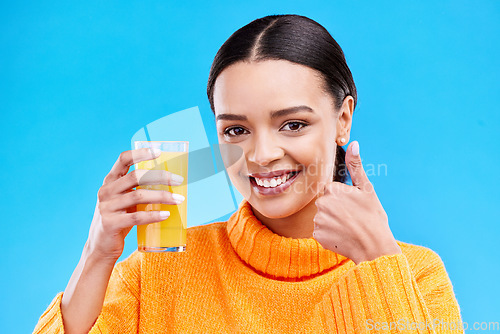 Image of Happy woman, portrait and thumbs up for orange juice in studio, blue background and yes emoji. Female model, drinking glass and good review of fruit cocktail for nutrition, vitamin c diet and detox