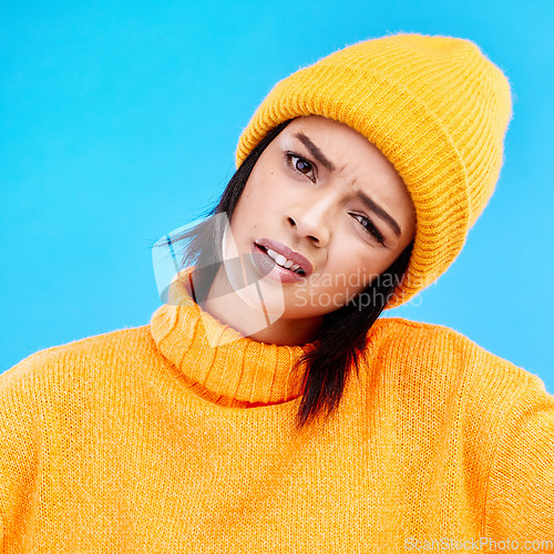 Image of Portrait of woman in winter fashion with confusion, beanie and doubt isolated on blue background. Style, funny expression on face and gen z girl on studio backdrop with warm clothing for cold weather