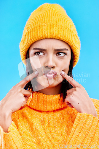 Image of Quirky, goofy and young female in a studio with a comic, funny and crazy face expression. Gen z, silly and beautiful woman model from Puerto Rico touching her cheeks isolated by a blue background.