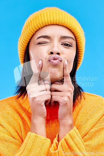 Image of Portrait of woman in winter fashion with kiss, beanie and happiness isolated on blue background. Style, face of happy gen z girl in studio with fun expression and warm clothing for cold weather.