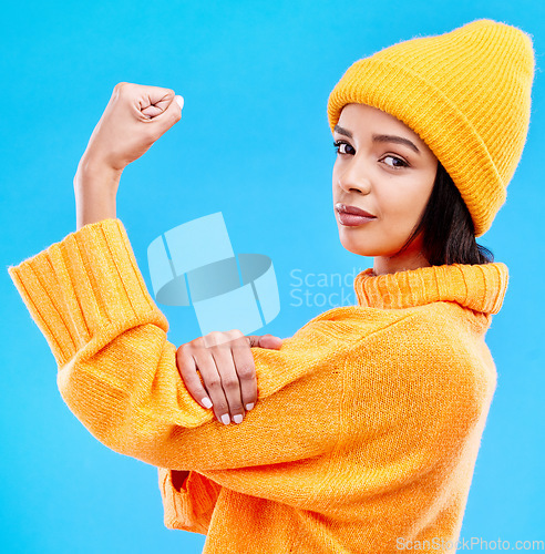 Image of Portrait of woman in winter fashion with power, beanie and glasses isolated on blue background. Style, arm flex and gen z girl in studio backdrop with strong face and warm clothing for cold weather.