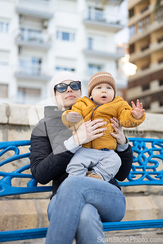 Image of Young mother with her cute infant baby boy child on bench in city park.