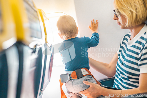 Image of Mom and child flying by plane. Mother holding and playing with her infant baby boy child in her lap during economy comercial flight. Concept photo of air travel with baby. Real people.