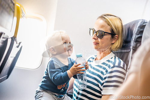 Image of Mom and child flying by plane. Mother holding and playing with her infant baby boy child in her lap during economy comercial flight. Concept photo of air travel with baby. Real people.