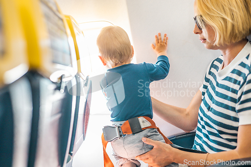 Image of Mom and child flying by plane. Mother holding and playing with her infant baby boy child in her lap during economy comercial flight. Concept photo of air travel with baby. Real people.