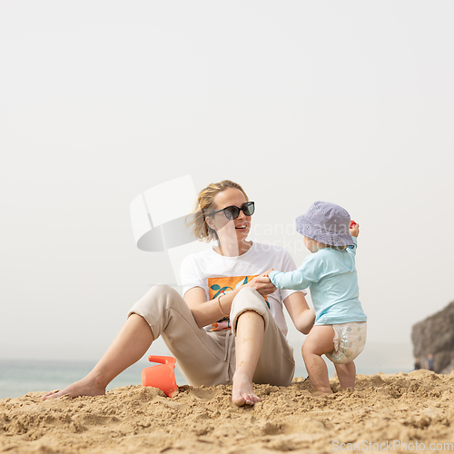 Image of Mother playing his infant baby boy son on sandy beach enjoying summer vacationson on Lanzarote island, Spain. Family travel and vacations concept.