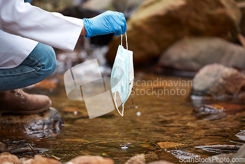 Image of Pollution, litter and face mask in river with hand of person for nature conservation, environment and safety. Covid, danger and trash with garbage in water for medical waste, healthcare and cleaning