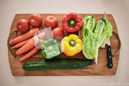 Image of Vegetables, cutting board and healthy food on the counter in the kitchen for a vegan meal. Crops, wood and diet with fresh, organic and natural produce with a knife for cooking a vegetarian dinner.