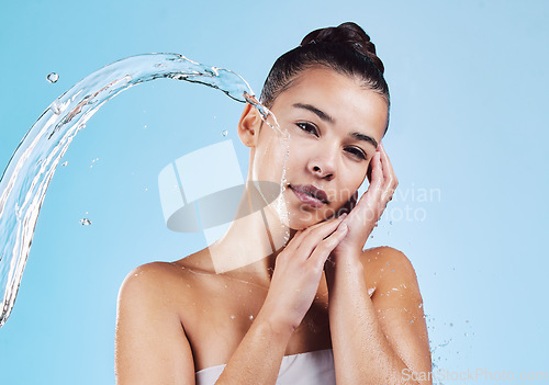 Image of Portrait, beauty and woman with water splash, cosmetics and cleaning against a blue studio background. Face, female model and person with drops, wellness and morning routine for self care and health