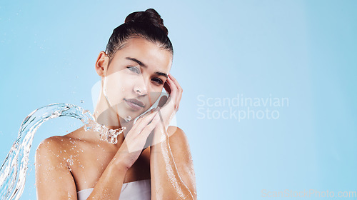 Image of Portrait, dermatology and woman with water splash, cleaning and beauty on a blue studio background. Face, female and person with clear liquid, morning routine and cosmetics for wellness and self care