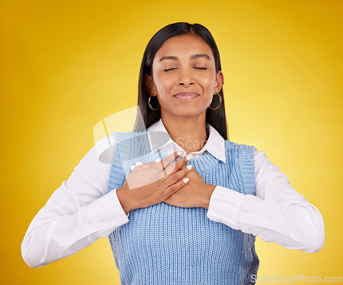 Image of Gratitude, peace and young female in a studio with her hand on her chest for a grateful expression. Mindfulness, smile and Indian woman model with thankful gesture isolated by yellow background.