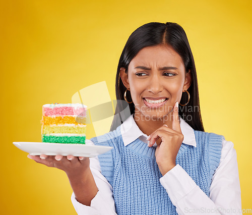 Image of Upset woman, rainbow cake and studio while thinking of birthday celebration, disaster or mistake. Face of Indian gen z female with dessert food with color, foul smell or bad idea on yellow background