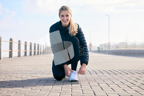 Image of Portrait, shoelace and happy woman runner at beach with performance, preparation or warm up. Fitness, shoes and face of girl with positive, mindset or smile before run, training and workout exercise