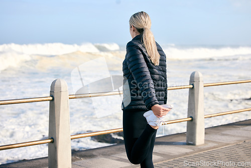 Image of Stretching legs, fitness and a woman at the beach for running, exercise and getting ready for cardio. Back, ocean and a runner preparing to train for sport or an outdoor workout with a warm up