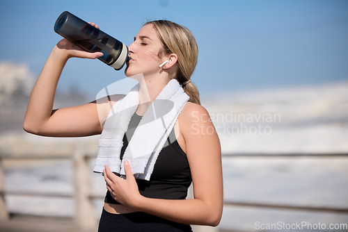 Image of Fitness, music and woman drinking water at the beach for sports, running and cardio routine. Podcast, bottle and thirsty female runner relax on workout break while streaming online motivation track